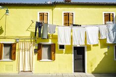 clothes hanging out to dry in front of a yellow building with windows and shutters