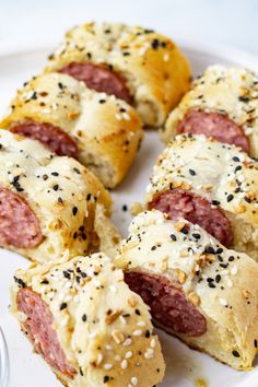 hot dogs wrapped in bread and sprinkled with sesame seeds on a white plate