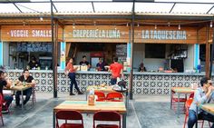 people are sitting at tables in front of a small restaurant with food on the counter