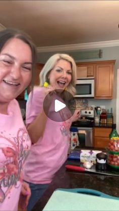 two women standing in a kitchen with food on the counter and one woman holding up her hand