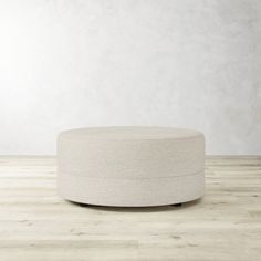 a round ottoman sitting on top of a hard wood floor next to a white wall