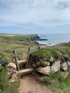 a wooden bench sitting on top of a lush green hillside next to the ocean with rocks and grass