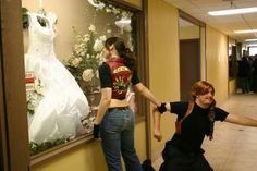 two people standing in front of a window with dresses hanging on the windowsills