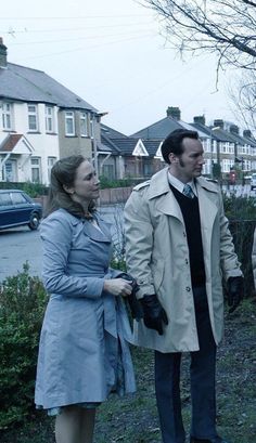 a man and woman standing next to each other in front of some houses on a street