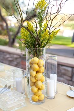 a vase filled with lemons on top of a table next to candles and flowers