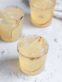 three glasses filled with drinks sitting on top of a white table covered in water droplets