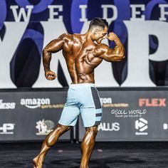 a bodybuilding competitor flexing his muscles on the stage at an event with words in the background