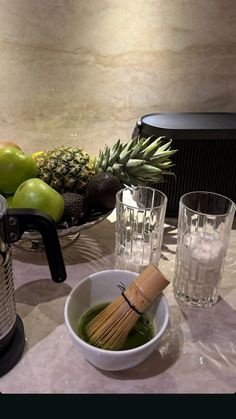 a bowl of green liquid next to two glasses and a pineapple on a table