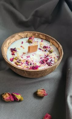 a wooden bowl filled with flowers on top of a gray cloth covered table next to a candle