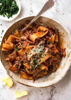 a bowl full of pasta with meat and parmesan cheese on the side, next to a spoon