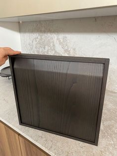 a person holding up a black framed object on top of a kitchen counter with a stove