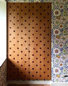 a wooden cabinet sitting in the corner of a room next to a wall with flowers on it