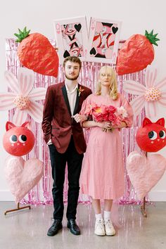 a man and woman standing next to each other in front of a wall with pink decorations