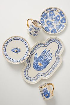 three blue and white dishes with gold handles, one holding a hand print on it