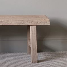 a wooden bench sitting on top of a carpeted floor next to a gray wall