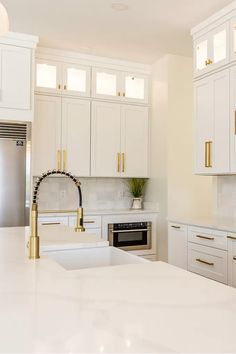 a kitchen with white cabinets and gold handles