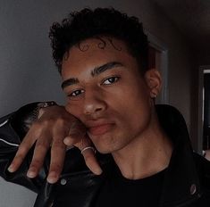 a young man with curly hair and piercings poses for the camera, wearing a black leather jacket