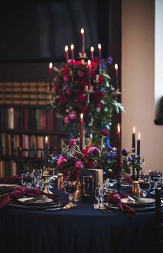 the table is set with candles, plates and flowers in front of bookshelves