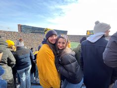 two women hugging each other in front of a crowd at a football game on a sunny day