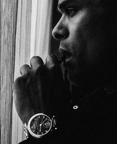 a black and white photo of a man with a watch on his wrist looking out the window