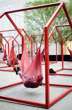 two people laying in hammocks suspended by red metal frames on the ground outside