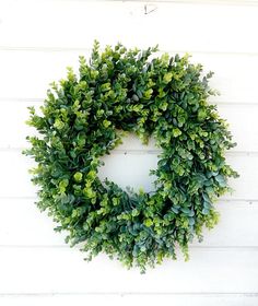 a green wreath hanging on the side of a white wall with wood planks behind it