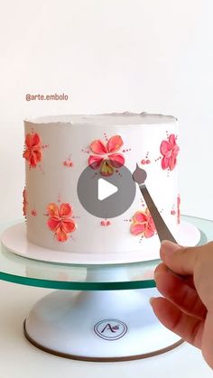 a person cutting into a white cake with pink flowers on it and a video player in the background