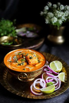 a bowl of soup on a plate with onions and limes