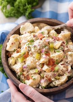 two hands holding a wooden bowl filled with potato salad