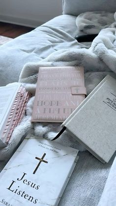 a bed with two books and a cross on top of it next to some blankets