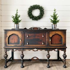 two potted plants sit on top of an old wooden cabinet in front of a wreath