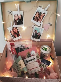 an open box filled with pictures and other items on a table next to string lights