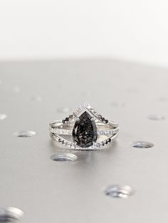 a black and white diamond ring sitting on top of a silver surface with drops of water around it