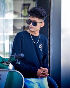 a young man wearing sunglasses sitting on top of a green scooter in front of a building