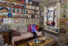 an older woman sitting on a couch in a living room filled with furniture and bookshelves