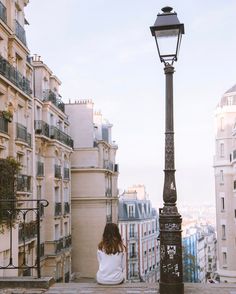 a woman sitting on the ground next to a lamp post in front of some buildings