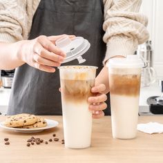 a person pouring coffee into two cups on top of a wooden table next to cookies