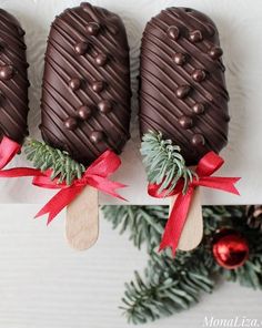 three chocolate covered pops are sitting on a white plate with red bows and pine cones