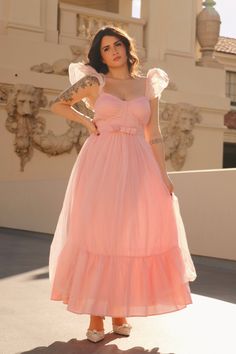 a woman in a pink dress poses for the camera with her hands on her hips