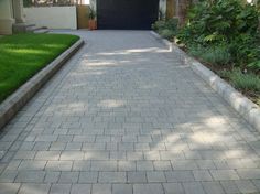 a driveway with grass and bushes in the background