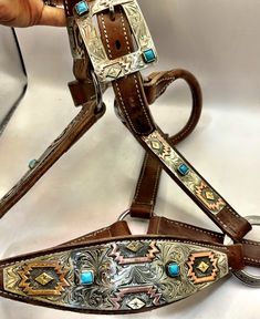 a person is holding up a brown leather dog harness with turquoise stones on the sides