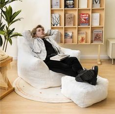 a man sitting in a white chair with his feet up on the floor while reading a book