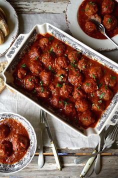 meatballs in tomato sauce and bread on a table with utensils, forks and spoons