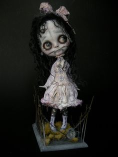 a creepy doll with long hair standing on top of a wooden block in the dark