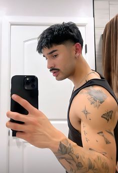 a man with tattoos taking a selfie in front of a mirror holding a cell phone