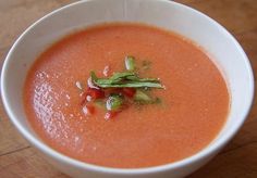 a white bowl filled with tomato soup and garnished with green leaves on top