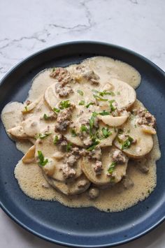 a blue plate topped with ravioli covered in meat and cheese sauce on top of a marble table