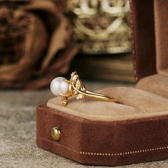 a gold ring with a white pearl sits in a velvet box