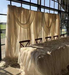 four wooden chairs sitting in front of a window covered with sheer curtains and drapes