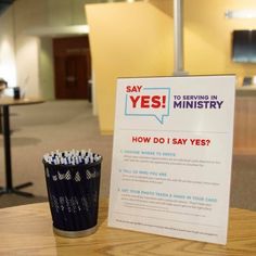 a sign sitting on top of a table next to a cup filled with pencils